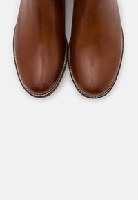 Une paire de chaussures de ville en cuir brun poli avec des orteils arrondis et des semelles cousues sur un fond blanc uni.