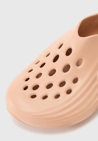 Dichte schoen in zacht blushroze materiaal met meerdere ronde ventilatiegaten en getextureerde ribbels langs de zijkanten.