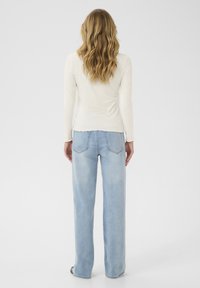 Witte ribgebreide top met lange mouwen, gecombineerd met lichtblauwe wijde jeans. De top heeft een cropped zoom en delicate, pluizige randen.