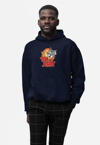 Felpa blu navy con una grafica di Tom e Jerry. Vestibilità classica con tasca frontale e cappuccio regolabile, realizzata in tessuto morbido.
