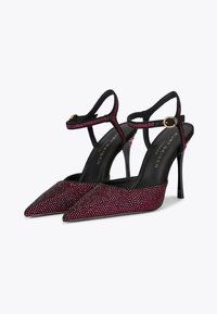 Tacchi a stiletto neri e rosa con punta affilata, adornati con piccole strass, dotati di una cinghia alla caviglia con dettagli in oro.