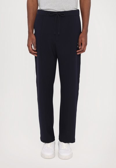 Pantalons de jogging pour hommes en marine avec une taille à cordon, poches latérales et logos blancs ; tissu lisse et coupe ajustée avec un ourlet à poignets.