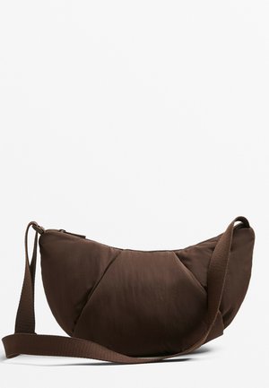 Brown padded crossbody bag with a rounded shape, sturdy fabric, angled seams, and a woven strap, featuring a zip closure and minimal hardware.