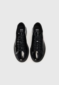 Baskets en cuir verni noir avec un bout arrondi, un design à lacets et une semelle en caoutchouc, avec une marque sur la langue et sur le côté.