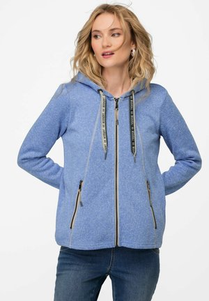 Sweat à capuche zippé bleu clair en tissu texturé, avec une capuche, des cordons de serrage noirs et deux poches zippées à l'avant.