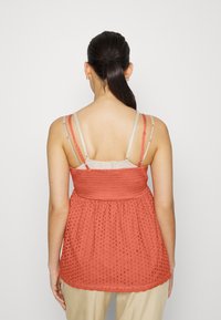 Koralinė medvilninė tank top su raukinių liemeniu, laisva forma ir tekstūruotu taškų raštu, turi reguliuojamus petnešas ir banguotą apatinę dalį.
