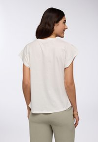 T-shirt color crema con maniche a cappuccio, vestibilità ampia e orlo arrotondato. Tessuto texturizzato abbinato a pantaloni verde oliva chiaro.