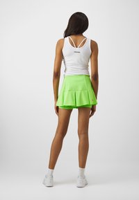 Jupe plissée verte avec une taille haute, fabriquée en tissu léger. Accompagnée d'un débardeur blanc arborant un logo au dos.