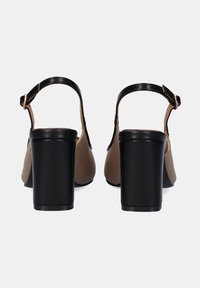 Sandalias de tacón alto marrones con un tacón de bloque negro, correa de tobillo ajustable y acabado de cuero suave. Diseño minimalista y forma estilizada.