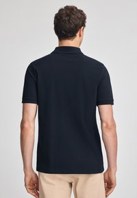 Svart polo skjorta med klassisk krage och korta ärmar, har en slät textur i en figurnära design, bärs med khakifärgade byxor.