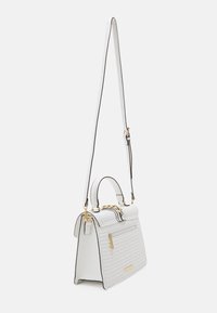 Hvid quiltet håndtaske med guldhardware, et håndtag øverst og en justerbar skulderrem; har en frontlomme med lynlås og kontrasterende sort kant.