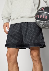 Sorte atletiske shorts med et subtilt geometrisk mønster, lavet af letvægtsmateriale. Har en elastisk talje og sort kant.
