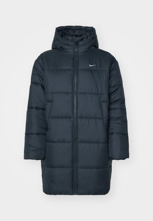 Puffer jacket in dark navy, featuring a hood, full front zipper, ribbed cuffs, and quilted design with horizontal stitching. Nike logo on chest.