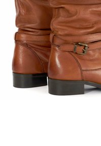 Bottines en cuir marron avec une texture lisse, dotées d'un accent à boucle sur le côté et d'un bout arrondi, sur un petit talon noir.