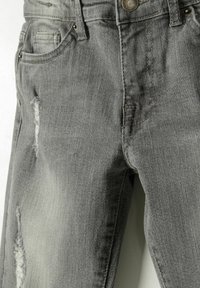 Harmaa denim farkut, joissa on kulutettuja kohtia, viisi taskua ja nappikiinnitys vyötäröllä. Rikkaita kuituja ja haalistunut pinta.