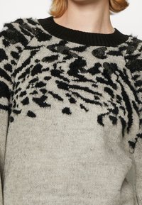 Knit sweater in light gray with a black animal print design. Features a ribbed black crew neckline and soft texture.