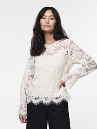 Kanten blouse in off-white met lange mouwen, een gegolfde zoom met franjes en bloempatronen. G gedragen met donkere broeken.