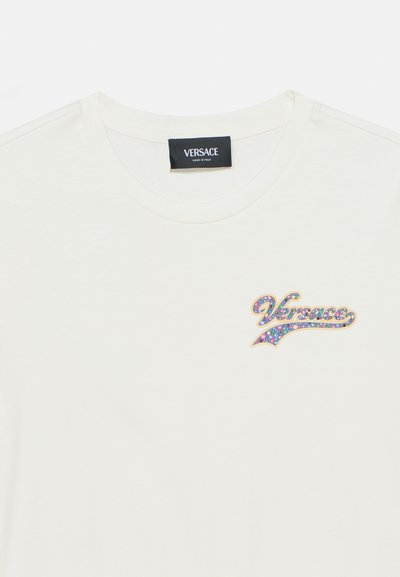 Άσπρη βαμβακερή μπλούζα με στρογγυλή λαιμόκοψη, με κεντημένο πολύχρωμο λογότυπο «Versace» από στρας στο αριστερό μέρος του στήθους.