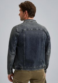 Veste en denim bleu foncé avec une coupe classique, poignets boutonnés et détail au niveau de l'empiècement du dos. La texture délavée ajoute un intérêt visuel.
