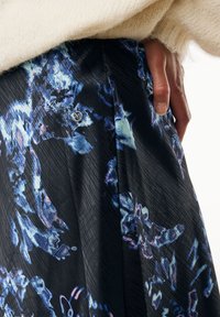 Falda negra con un patrón floral en azul y púrpura, con una textura sutil. Incluye un pequeño acento de logo metálico cerca de la cintura.