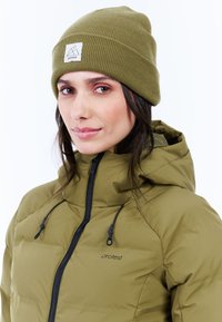 Olivgrüne Pufferjacke mit hohem Kragen, schwarzem Reißverschluss und verstellbaren Zugbändern. Begleitet von einer passenden gerippten Mütze mit Logopatch.