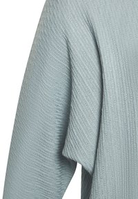 Helles blaues gestricktes Gewebe mit diagonaler Rippstruktur und sichtbaren Nähten an einem Ärmel.