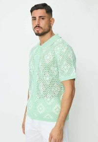 Polo en maille vert menthe avec un motif en losanges, doté d'un devant à boutons et de manches courtes. Texture légère et respirante.