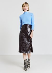 Hellblau gestrickter Pullover mit hohem Kragen, braune glänzende Leder-Midirock mit seitlichem Schlitz und Schlangenmusterschuhen bis zu den Knöcheln.