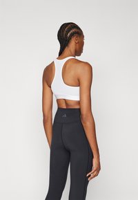 Witte sportbh met een racerback ontwerp, gecombineerd met hoogtaille zwarte leggings met een subtiel logo en een gladde textuur.