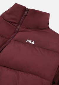 Giacca a vento bordeaux con colletto alto, chiusura frontale con zip e logo FILA bianco sul petto; texture liscia e design trapuntato.