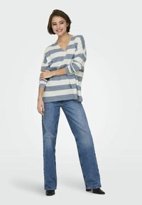 Top a righe a maniche lunghe in crema e azzurro chiaro, con scollatura a V e vestibilità rilassata. Abbinato a jeans a gamba larga blu e stivaletti neri.