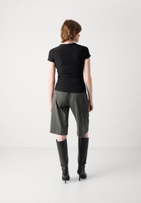Svart teksturert topp med korte ermer, kombinert med olivengrønne skreddersydde shorts og knelerange svarte støvler. Glatt stoff med tettsittende design.