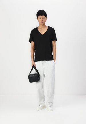 Tricou din bumbac negru cu decolteu în V, pantaloni de trening gri deschis, adidași albi și o geantă mică neagră tip crossbody. Design simplu, croială lejeră.