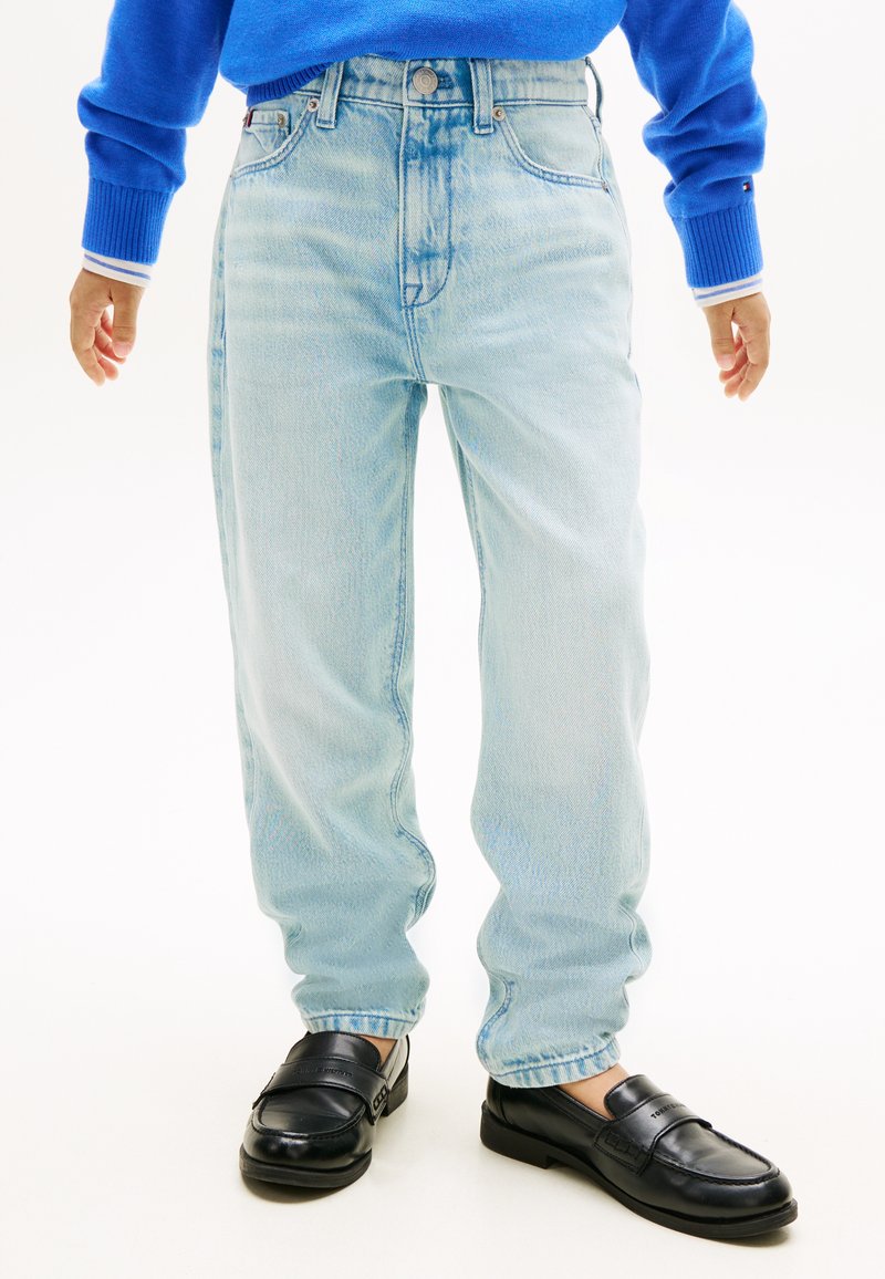 Άτομο που φοράει ανοιχτό μπλε κοντές τζιν, μαύρα μοκασίνια και μπλε πουλόβερ με μανσέτες με λευκές ρίγες.