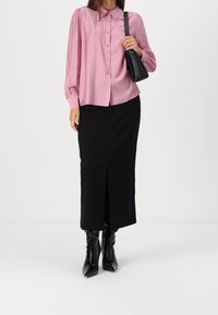 Chemisier boutonnière rose clair à manches longues avec épaules bouffantes, associé à une jupe noire longueur genoux avec fente devant et des bottes noires jusqu'aux genoux.