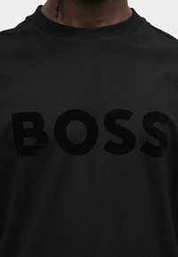 Μαύρο βαμβακερό t-shirt με υφασματικό λογότυπο "BOSS" σε πιο σκούρο χρώμα. Στρογγυλή λαιμόκοψη και κοντά μανίκια. Απλός, κλασικός σχεδιασμός.