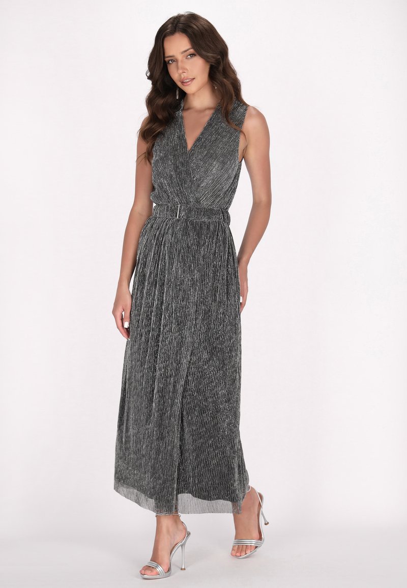 Maxime dress in a black and silver pleated design, featuring a deep V-neck, belted waist, and a smooth texture; combined with silver heels.