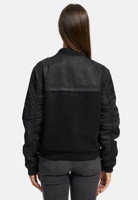 Black bomber jacket featuring a combination of smooth and textured materials, ribbed cuffs, and a distinctive back panel design.