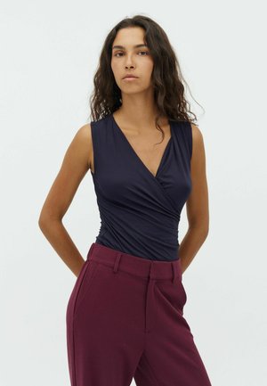 Top senza maniche blu navy con design avvolgente; materiale morbido con trama visibile. Abbinato a pantaloni borgogna a vita alta.