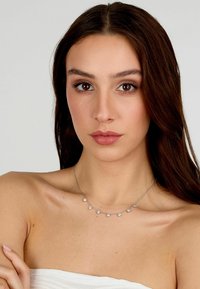Collana in argento con cinque gemme trasparenti, ciascuna incastonata in una montatura a griffe, che mostra un design raffinato. Texture metallica liscia.