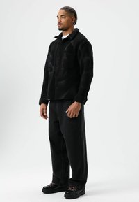 Zwarte fleecejas met knopen, twee borstzakken, gecombineerd met wijde zwarte jeans en zwarte veterlaarzen met roze accenten.