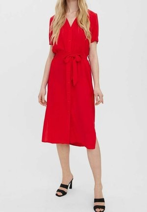 Robe rouge à boutons avec des manches courtes, détail de taille nouée, longueur au genou et texture lisse. Sandales à talons noires.