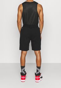 Černý bezrukávový top s texturovaným povrchem, spárovaný s černými šortkami. Nosené s vzorovanými šedými ponožkami a červenými a černými vysokými teniskami.