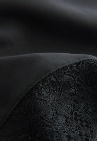 Gros plan sur un tissu noir à texture lisse drapé sur des détails en dentelle florale noire.