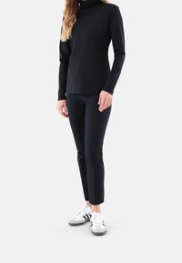 Schwarzes langärmliges Rollkragenoberteil, kombiniert mit eng anliegenden schwarzen Hosen und weißen Sneakern mit schwarzen Streifen und grauen Akzenten an der Sohle.