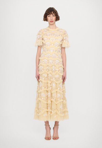 Robe jaune à volants en dentelle avec des embellissements floraux et des manches à volants. Longueur jusqu'à la cheville, corsage ajusté avec un motif festonné.