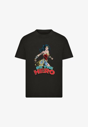 Black t-shirt featuring a graphic of a female superhero, with colorful comic-style text “BE THE HERO” in red and blue accents.