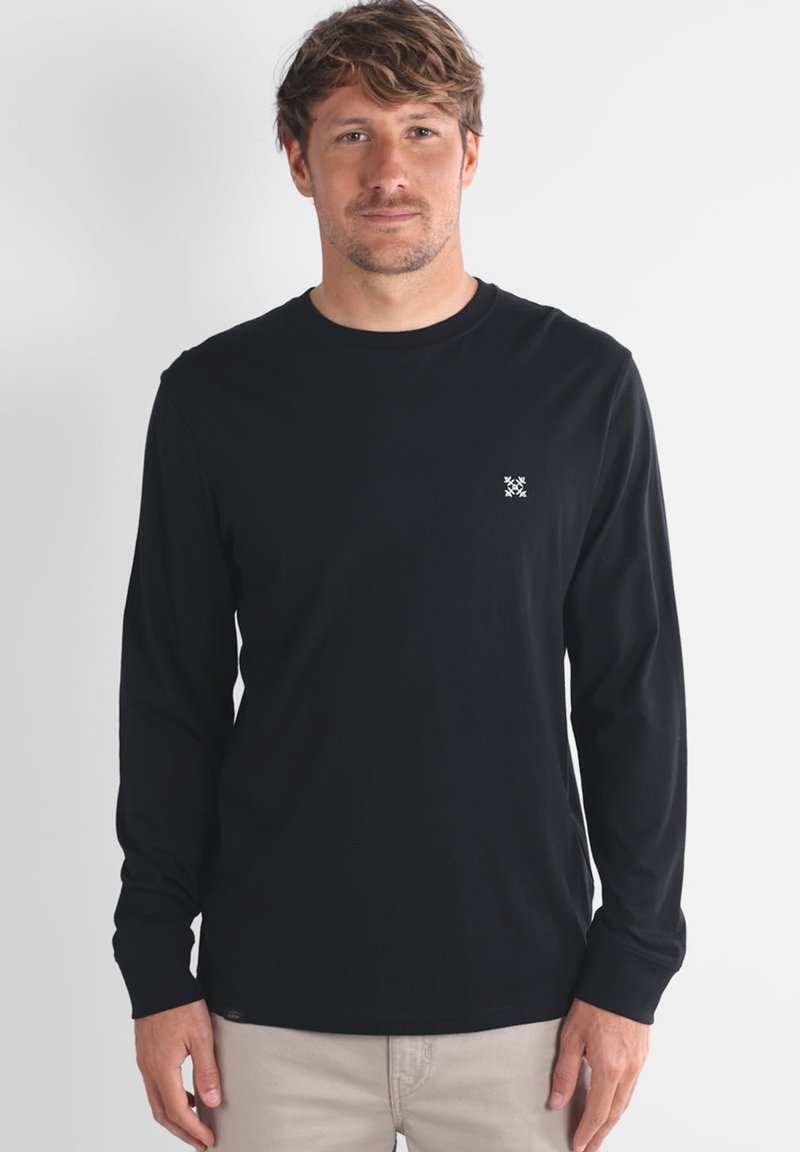 Chemise noire à manches longues en tissu lisse avec un col rond et un petit logo blanc sur la poitrine.