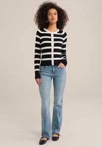Cardigan a righe bianche e nere con bottoni, design aderente, texture morbida. Abbinato a jeans azzurri a zampa d'elefante e ballerine nere.