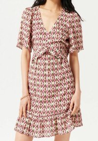 Blommönstrad klänning med V-ringning, korta ärmar och volangkant. Färgerna inkluderar rosa, grön och vit i ett diamantmönster.